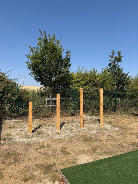 Two sets of timber posts holding steel pull-up and traverse bars at different heights, on a gravel base beside the field.