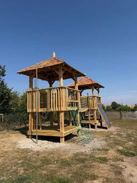 Close view of the first tower: a hexagonal cedar shingle roof over an open deck with slatted timber balustrade, a green climbing net up one side and a grab pole at the front.