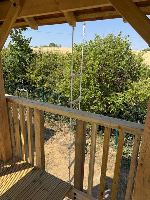 View out from a tower over the balustrade to a rope ladder hanging down to the ground, with hedge and fields beyond.