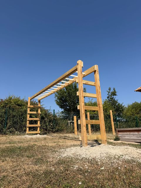 A timber monkey-bar frame with rungs sloping down to a low climbing ladder at one end.