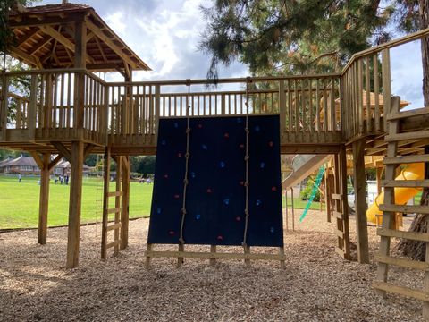 Climbing wall with coloured holds and two knotted ropes, set between two raised timber decks.