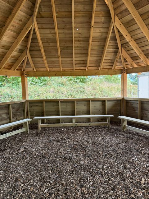 Inside the classroom: benches running round the walls beneath open window gaps, under the exposed timber roof.