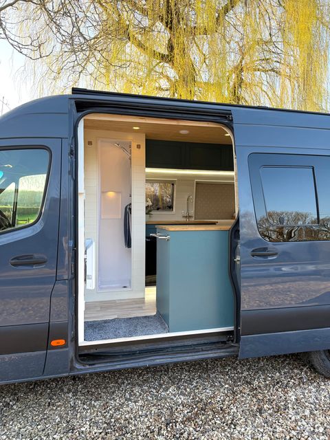 The open side door framing the interior, with the shower cubicle on one side and the teal kitchen units on the other.