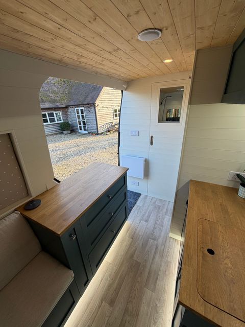 Looking forward past a chest of drawers and upholstered bench seat to the side door, with a mirrored wardrobe door alongside.