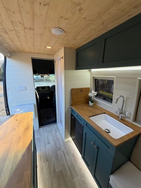 The galley: a deep white sink in an oak worktop with a chrome mixer tap, teal cabinets below, a fridge alongside and a window over the counter.