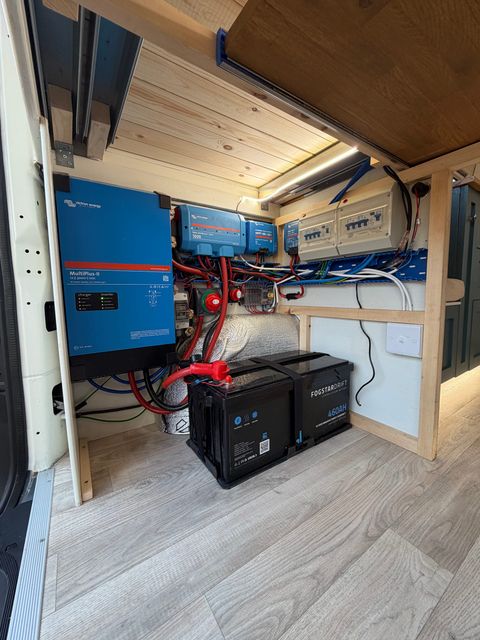 The electrical bay under the bed: a Victron inverter-charger and control units wired to a consumer unit, above two leisure batteries.