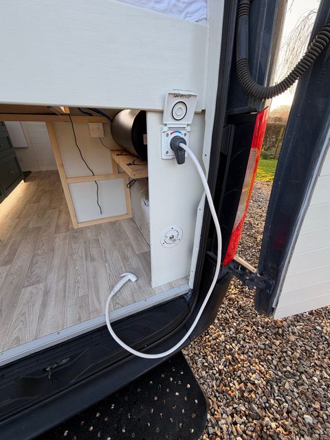 The external hook-up point in the door frame with a cable plugged in, and the under-bed storage bay visible inside.