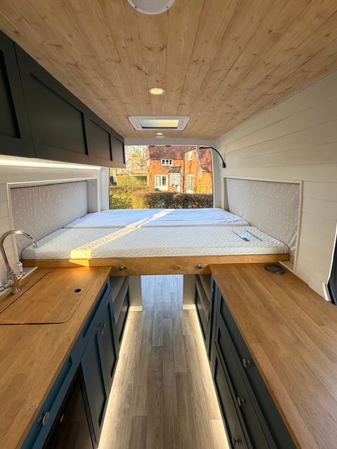 The rear bed with the back doors open onto a brick cottage, lit by the rooflight above and strip lighting under the units.