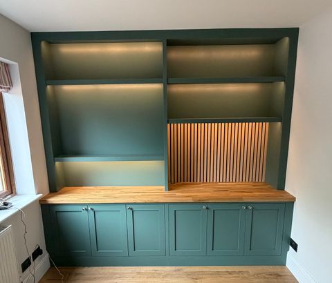 Fitted office cupboards in dark green with open shelving, an oak worktop and a slatted oak panel.