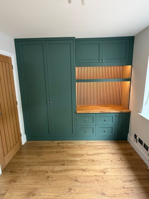The same room from the doorway, showing a full-height green wardrobe beside the desk run and drawers.
